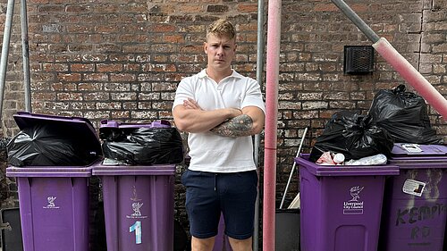 Cllr Carl Cashman standing in front of overflowing bins